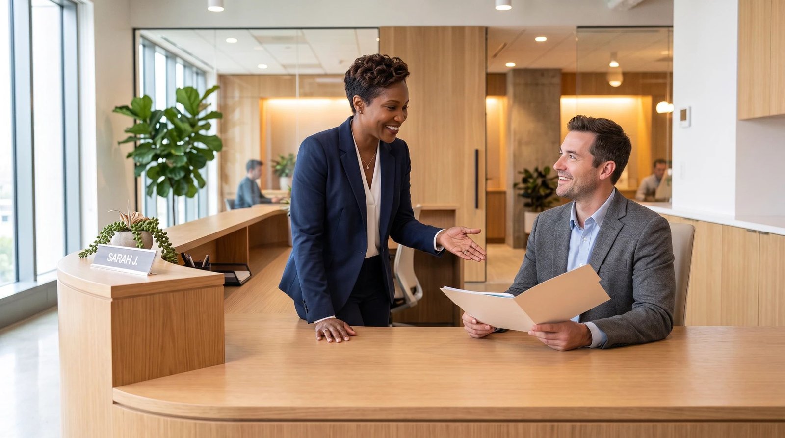 A receptionist welcoming a seated client holding a folder at a bright wooden front desk in a modern office